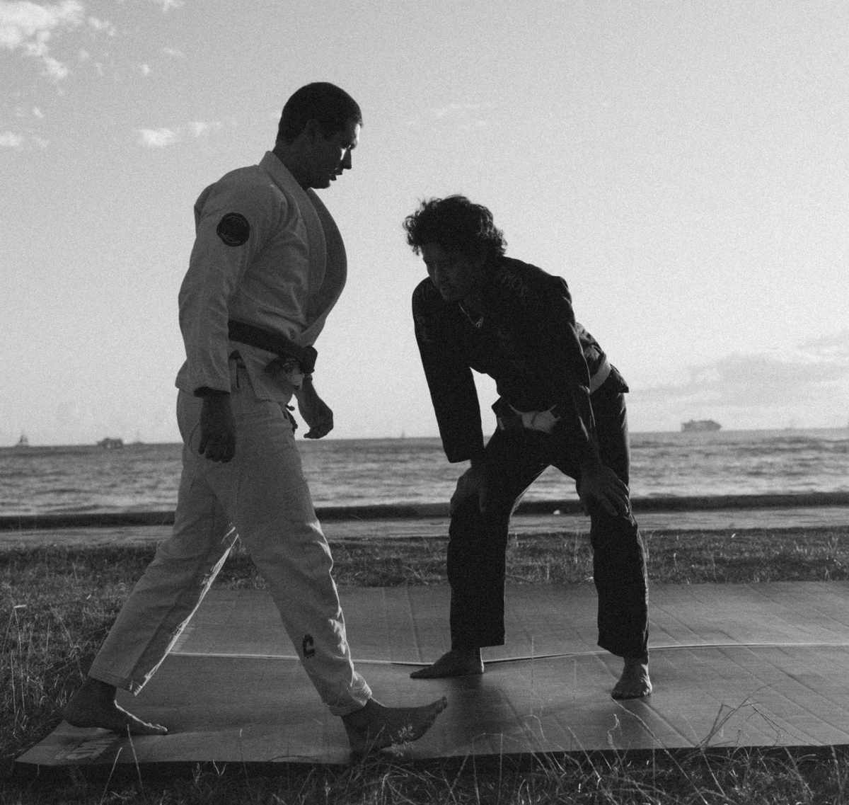 Two training partners squaring up on a mat by the ocean